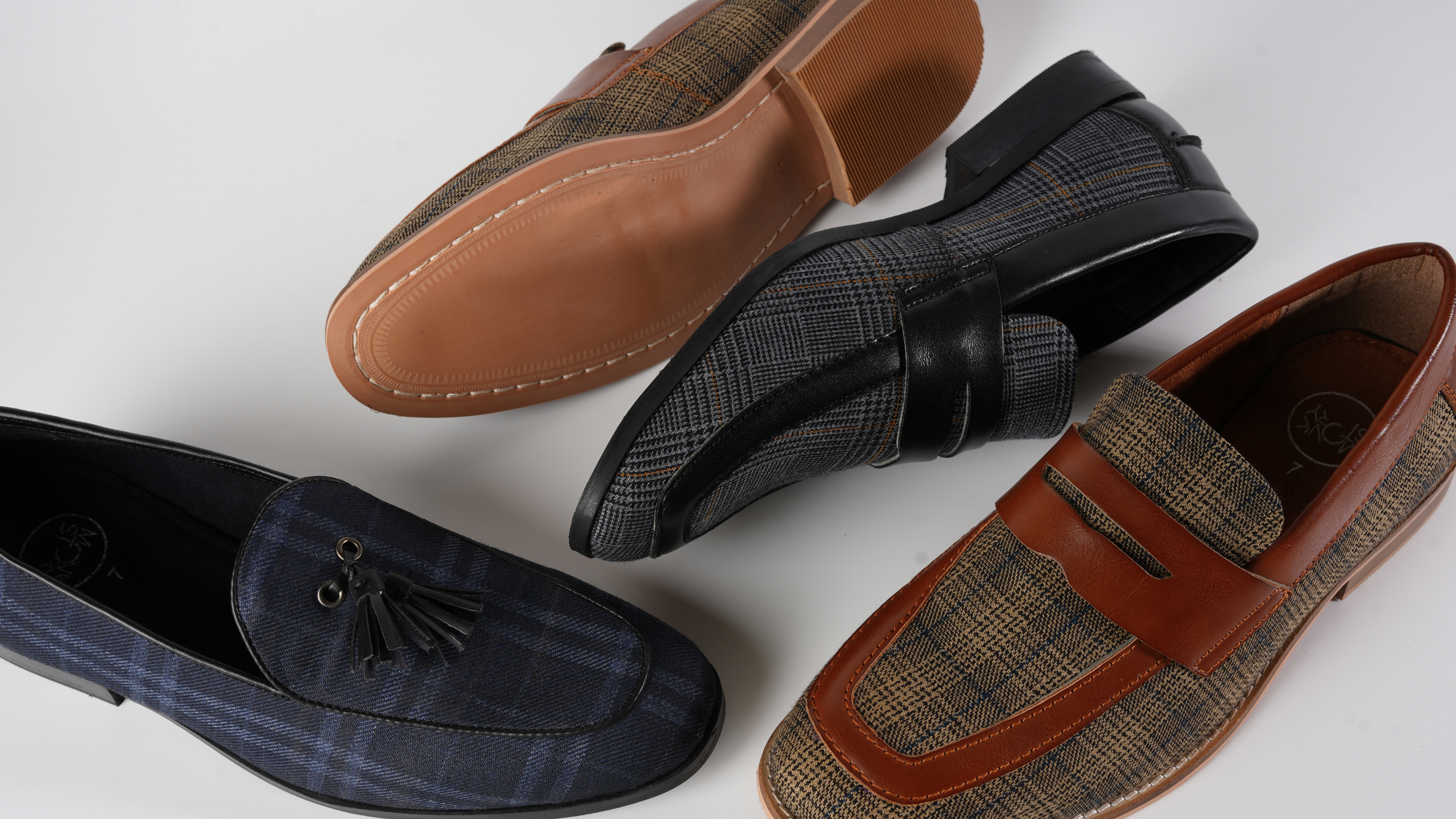 A collection of various men's shoes including loafers and dress shoes displayed in an overlapping arrangement on a white background.