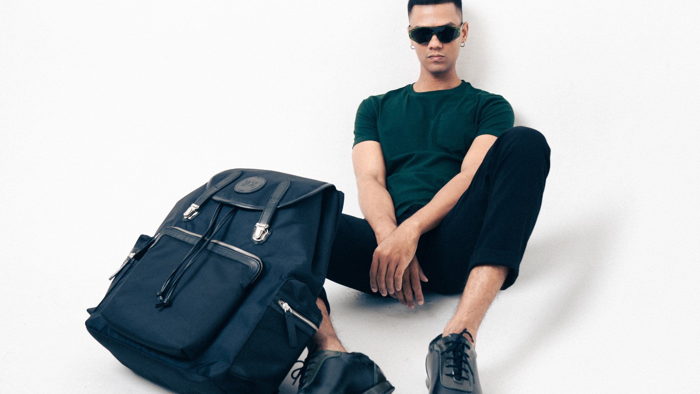 A man sitting on the floor with a backpack and sunglasses.